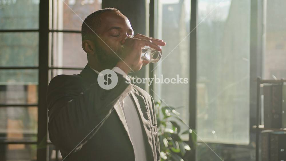 African American ethnic mature businessman senior man entrepreneur drink water glass of pure liquid in hot sun shining office feel thirsty