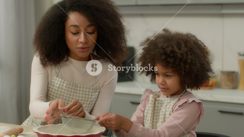 African American family cooking together mother woman mom teach little child kid girl daughter help mommy pour flour into sieve sift wheat