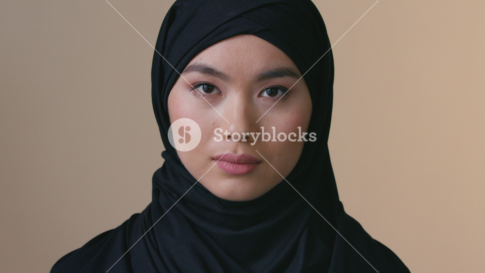 Portrait serious Asian Muslim woman wearing black hijab looking at camera indoor lonely sad female Islamic headscarf identity discrimination