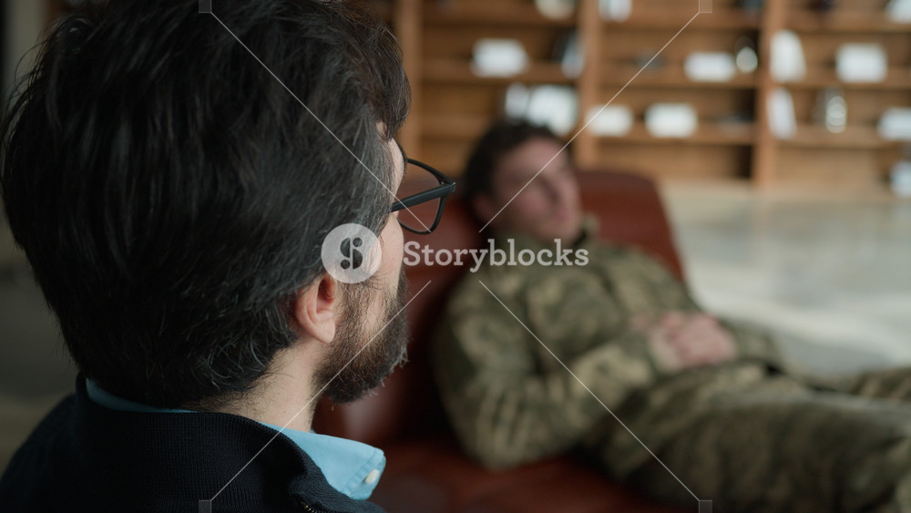 Middle aged Caucasian psychologist doctor man male speak talking to officer camouflage uniform military army soldier blurred patient guy