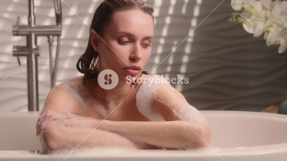 Calm attractive pretty Caucasian woman girl female relaxing in bubble foam bath tub enjoying peaceful self care routine spa at home bathroom