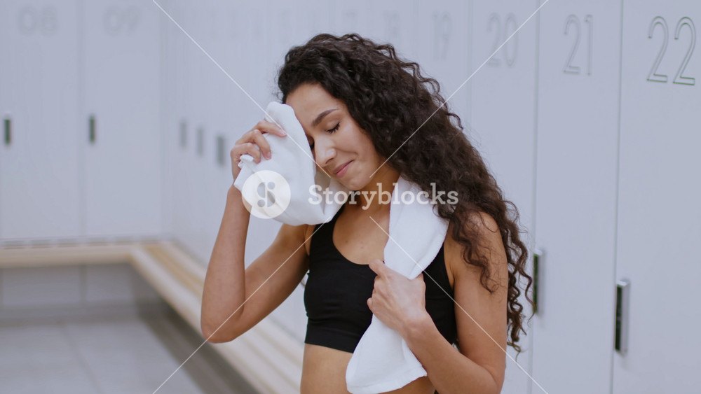 Smiling Young Hispanic Woman Drying Sweat With A Towel After Intense Workout, Standing In Gym Locker Room, Embracing Fitness Lifestyle And