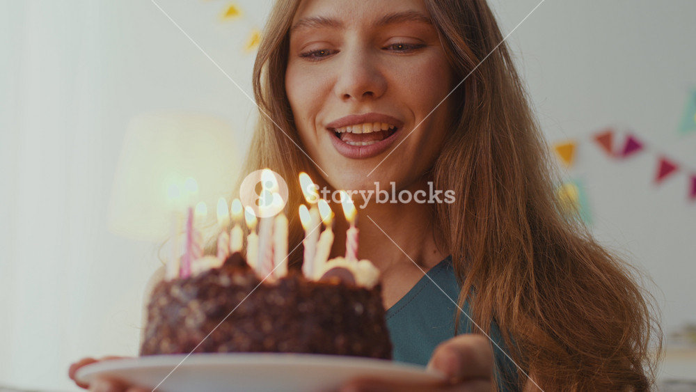A young woman with red hair smiles as she holds a birthday cake adorned with candles. The party takes place indoors, creating a festive