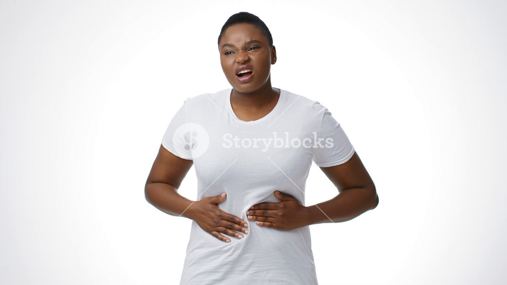 A millennial African American woman with short hair holds her stomach, expressing discomfort. She appears isolated, highlighting the