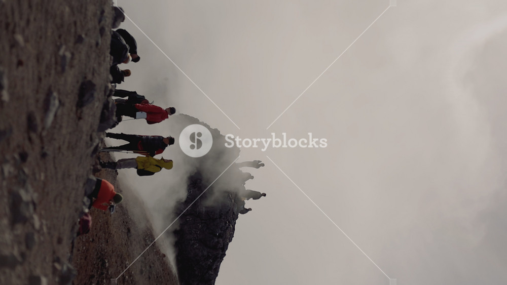 Kamchatka, Russia - August 24, 2025: Group of tourists relax on rim of steamy crater while man from another group takes pictures of