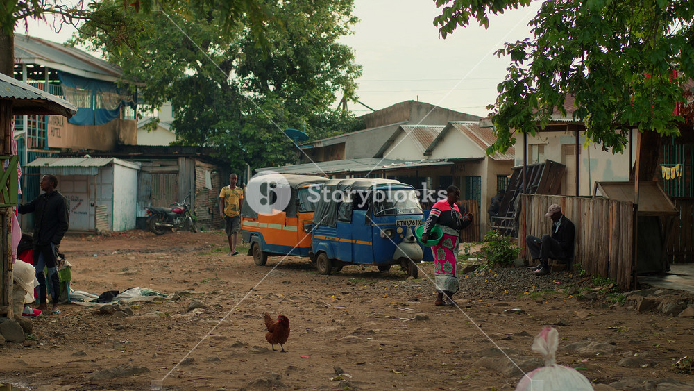 Kisumu, Kenya - June 6, 2025: African men and women goes in yard where parked three-wheeled small cars, motocycle and chickens walking