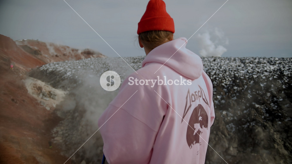 Kamchatka, Russia - August 24, 2025: Young man in red pants and pink hoodie stands on slope of volcano's crater and surveying landscape with