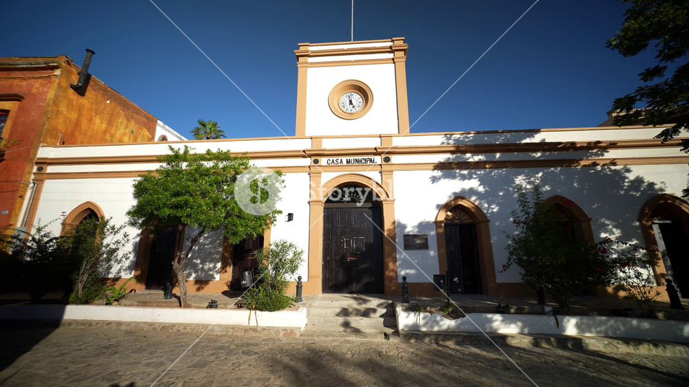 Camera pushing in to the beautiful exterior of white Municipal building with arched doorways in historical mining town of El Triunfo, Mexico.