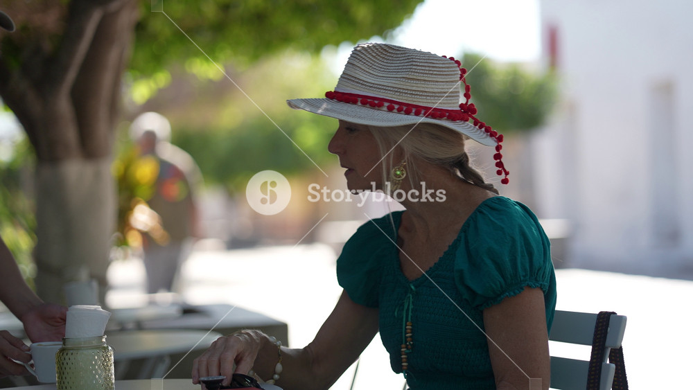 Senior woman tourist sits at cafe enjoying coffee and her phone near Loreto mission church while exploring Baja California Sur in Mexico.