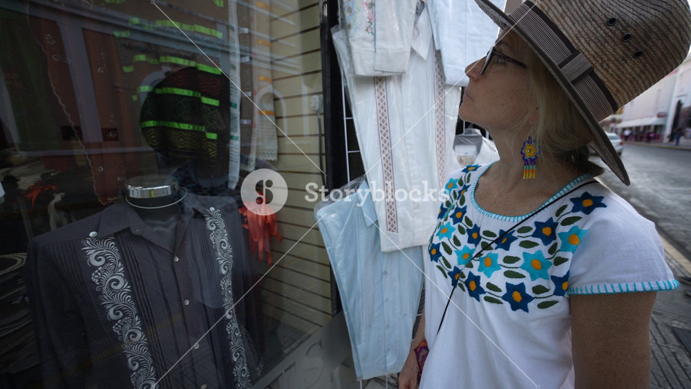Closeup of pretty mature senior woman tourist wearing ethnic clothes looking in window of tourist souvenir shop in Merida, Yucatan, Mexico.
