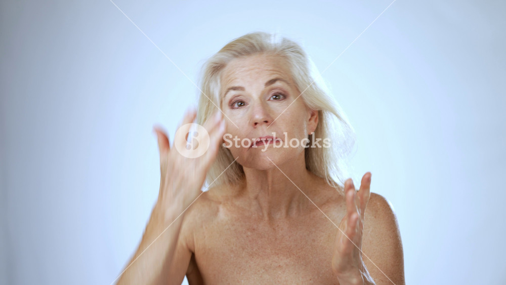 Portrait of happy 50s, 60s middle aged mature woman touching face skin applying face cream pampering. Old healthy dry skin care beauty concept, cosmetics and anti age plastic surgery.