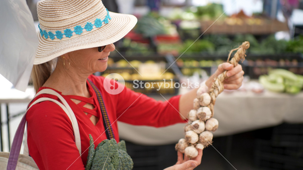 Mature woman smiles as she buys a braid of garlic at the Sonoma Farmers Market on a sunny morning in California