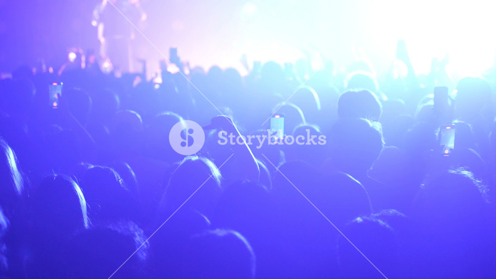 Unrecognizable fans dancing at a concert or festival party. Silhouettes of concert crowd in front of bright stage lights