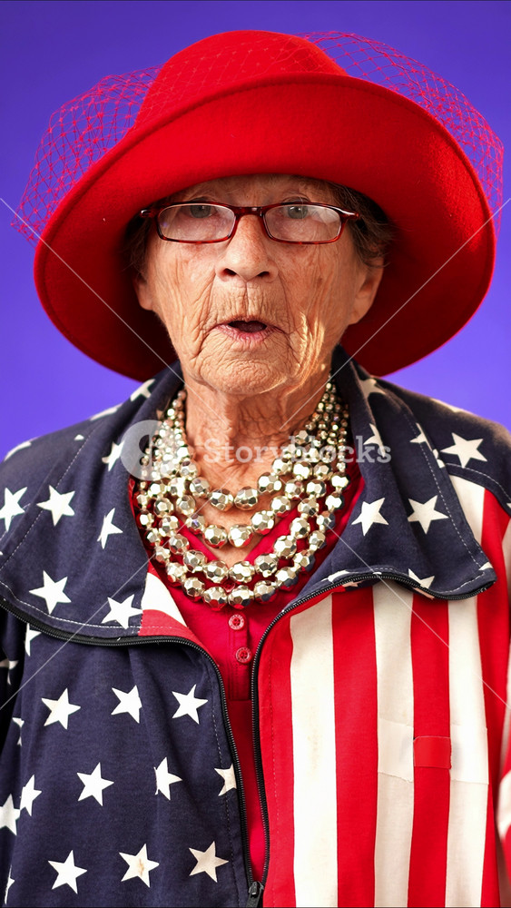 Vertical video funny portrait of smiling happy elderly toothless senior old woman with wrinkled skin smiling pointing to camera and giving call me gesture with hands isolated on solid purple background.