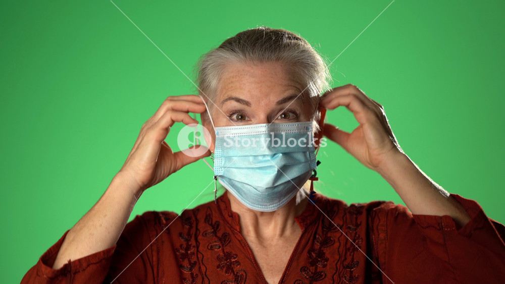 Woman takes off medical mask, vote earrings. Female breathes deeply and smiling looking at camera. Isolated on green screen background. Health care and medical concept. Close up portrait. 4k