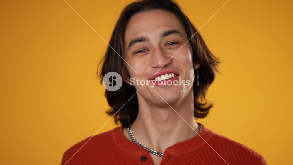 Slow motion portrait of happy handsome gender fluid Hispanic young man 20s wearing orange casual shirt isolated on yellow color background in studio.