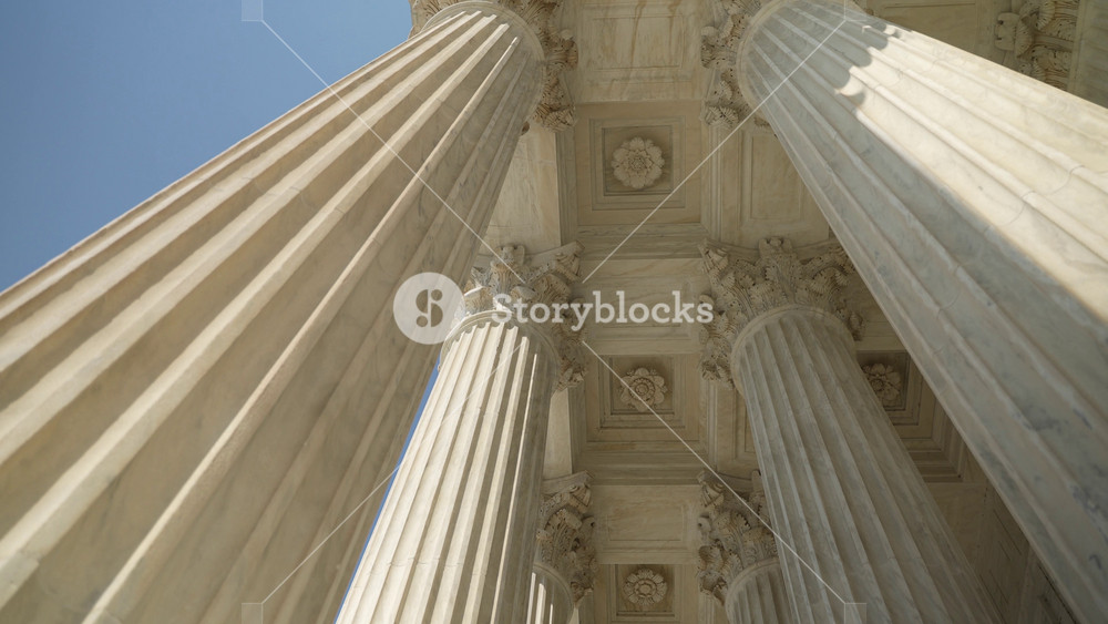Slow motion looking up at the top of Corinthian columns in front of US Supreme Court in Washington, DC, showing power over people and business.