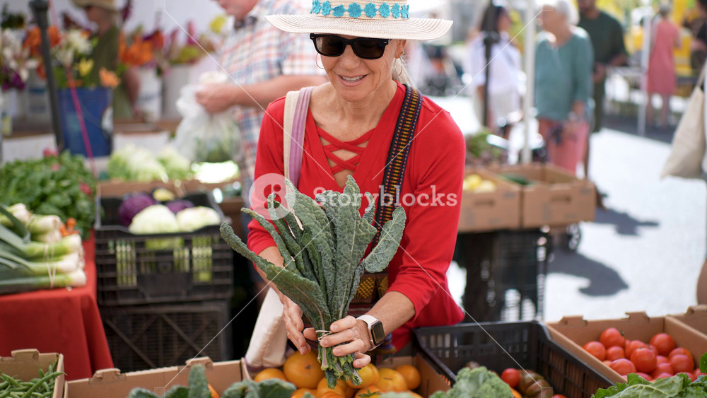 Happy senior woman purchases kale at the Sonoma Farmers Market on a bright day. The market is lively and colorful
