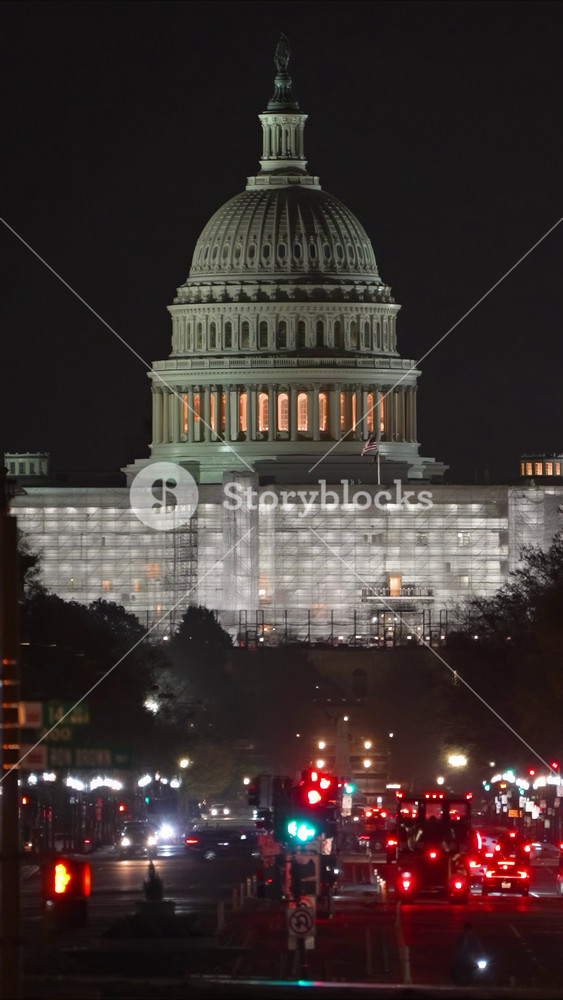 Vertical video view of the West side of the US Capitol building at night showing scaffolding for repairs and construction from Pennsylvania Avenue with traffic, in Washington DC