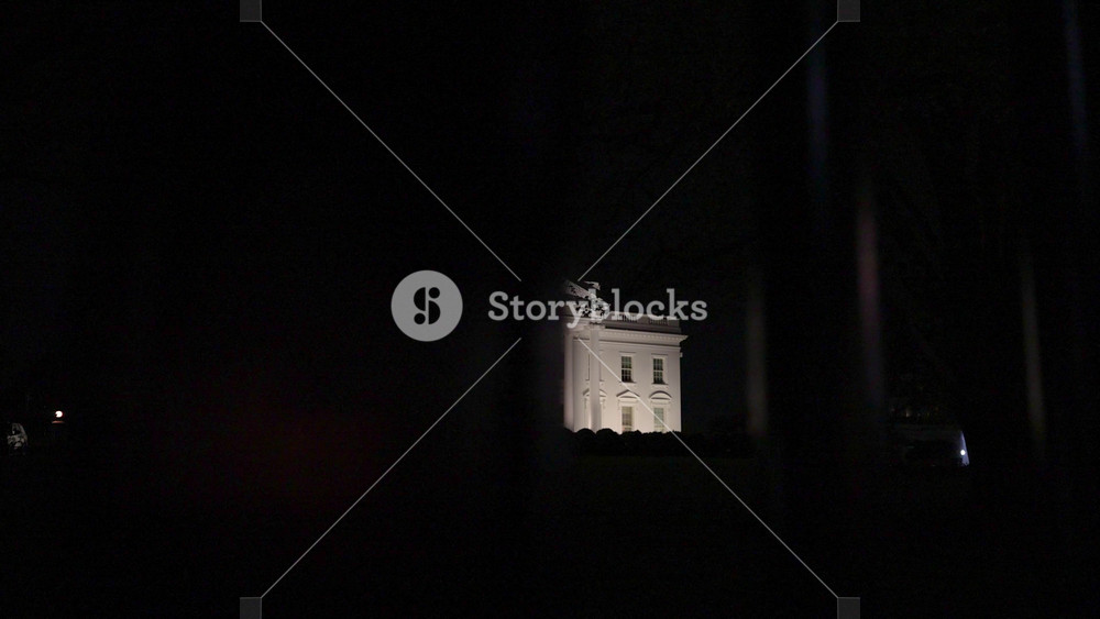 Wide angle slow motion to the right night view of the US Presidents home, the White House in Washington, DC. View through the iron bars in front on the South side.