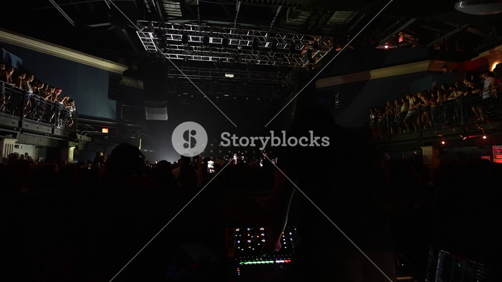 Unrecognizable fans dancing at a concert or festival party. Silhouettes of concert crowd in front of bright stage lights