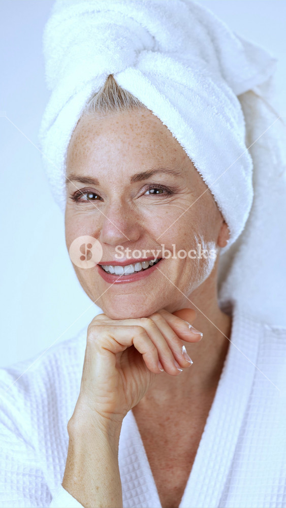 Vertical video portrait of attractive middle aged mature blond woman wearing bathrobe with natural makeup looking at camera. Advertising of perfect anti age skin care products, hotel spa services concept.