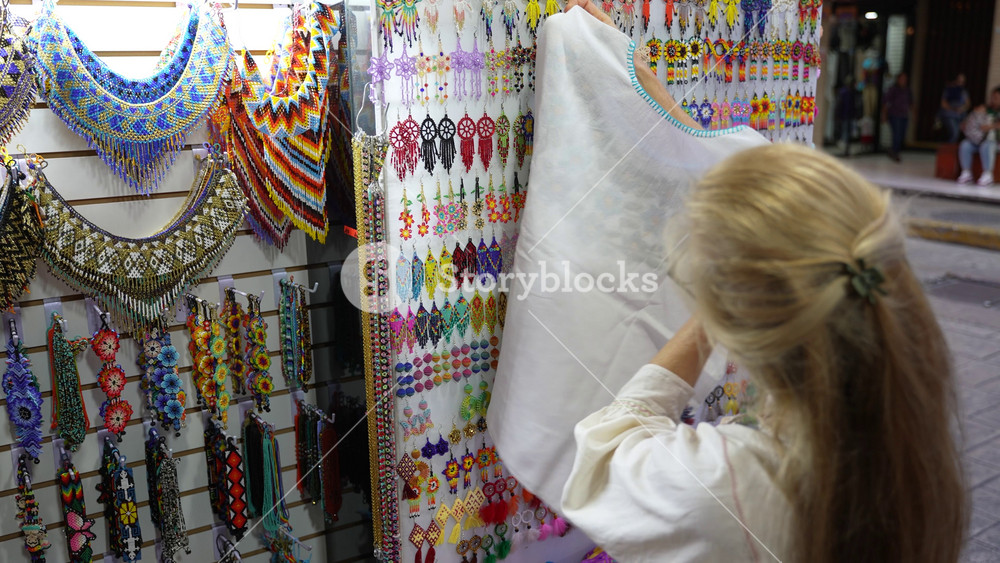 Mature woman tourist wearing ethnic clothes looking at locally made blouses in a souvenir shop in Merida, Yucatan, Mexico.