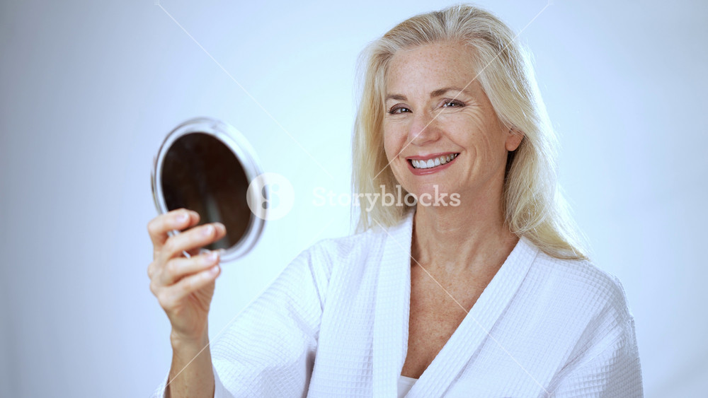Portrait of 50s, 60s, mature middle aged woman applying natural makeup powder foundation with cosmetic sponge on clean face skin smoothing wrinkles old lady looking in mirror beauty, white background