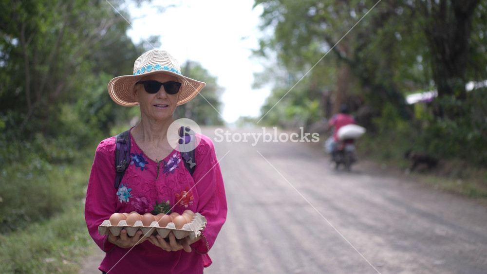 Mature woman walks down a dirt road in Nicaragua, balancing a tray of fresh eggs after visiting the local village market