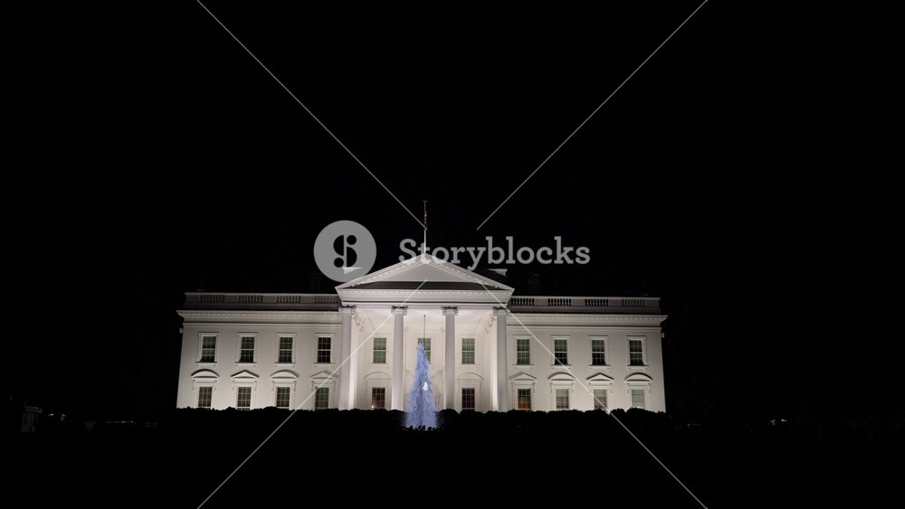 Static view at night of the US Presidents home, the White House in Washington, DC with blue water fountain in front. View through the iron bars on the South side.