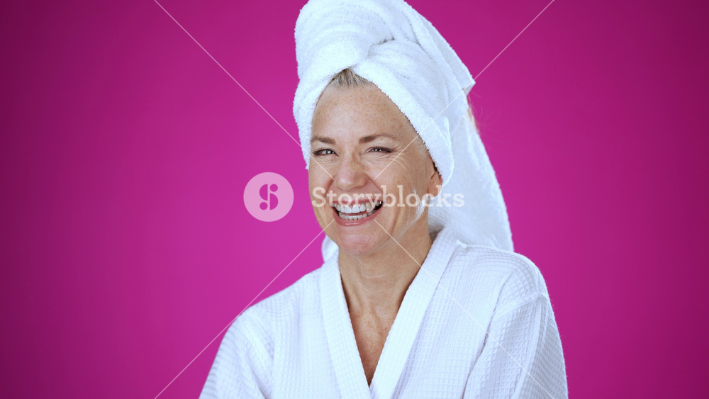 POV of smiling mature woman talking to camera holding phone recording vlog while at spa wearing bath robe. Gray-haired senior woman video calling in online chat using smartphone self portrait.