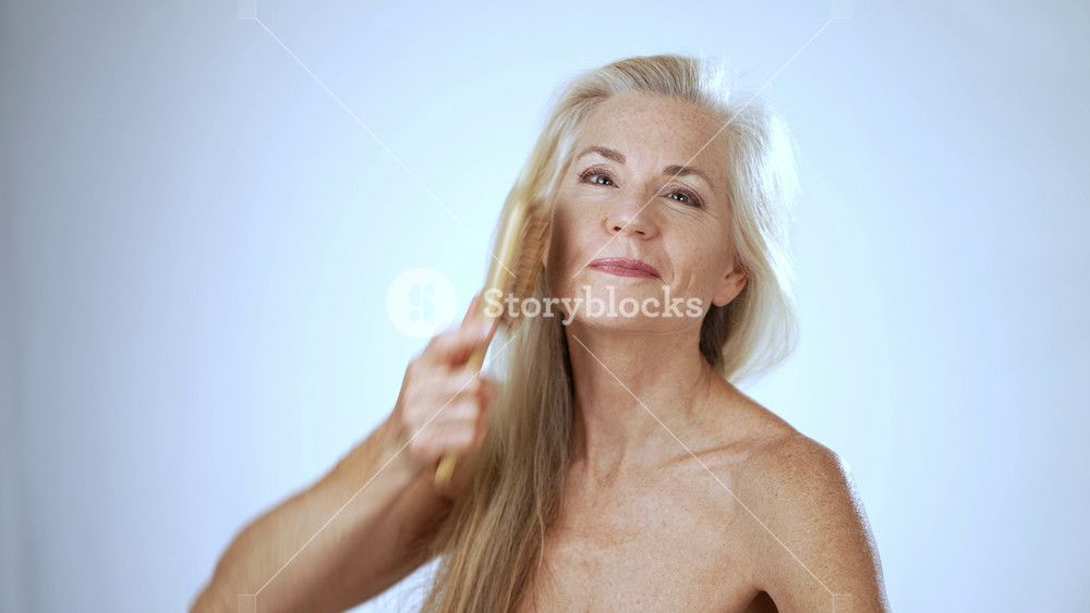 Portrait of happy Caucasian senior mature woman combing and playing with hair with hairbrush beautiful mature old lady brushing haircare studio background self care beauty routine cosmetic