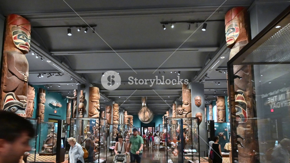 New York,USA, August 19, 2024. Visitors inside the Hall of Northwest Coast Indians at the Museum of Natural History, with 78 totem poles and a Haida canoe suspended from the ceiling in the background.