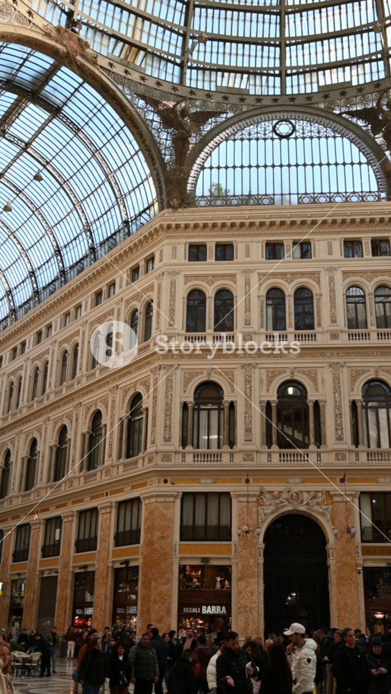 Naples, Italy, December 27, 2024. Vertical panning footage inside the Galleria Umberto I. People walking by, illuminated by natural light. Luxury shops and bars. Travel destinations.