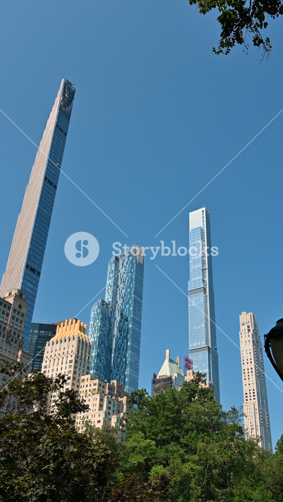 New York City, USA, August 14, 2024. Stunning vertical footage of skyscrapers framed by treetops in Central Park. Pan motion, beautiful summer day.