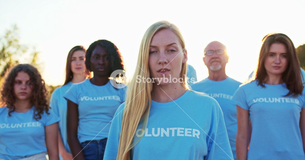Young attractive woman with a group of eco activists in the background. Pretty Caucasian female volunteer looking at camera and saying: I Am