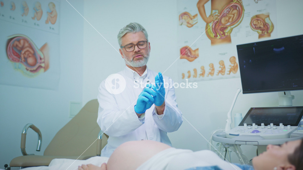 Caucasian male doctor wearing glasses putting on blue gloves preparing medical procedure. Professional following sanitary rules near