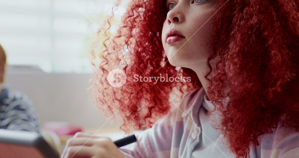 Attentive Caucasian girl listening carefully to teacher in middle of class. Child writing or drawing something with special pen on tablet