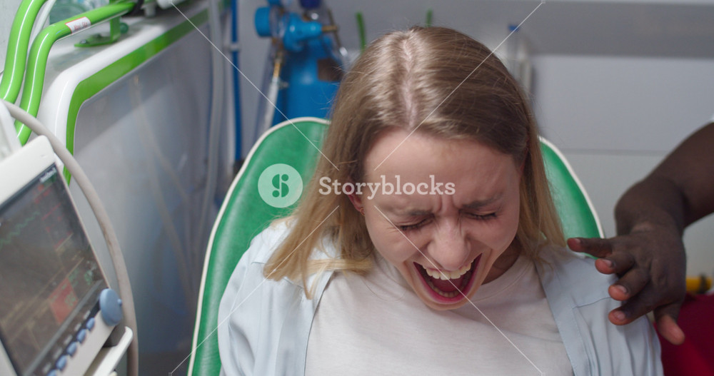 Caucasian young pregnant female in labor going to hospital with African American husband in ambulance. Woman in pain during giving child