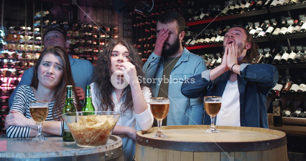 Upset company of Caucasian friends getting sad of favorite football team loosing in match in bar. Dissapointed men and women after watching