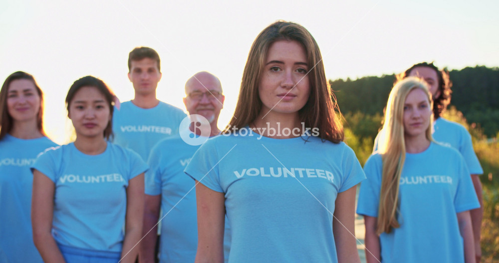 Portrait of attractive young woman with group of eco activists in background. Pretty Caucasian female volunteer looking at camera and saying