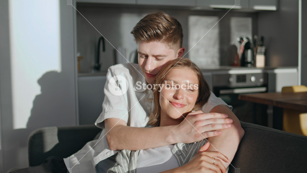 Happy sweethearts relax home in evening sunlight. Closeup loving man embracing beautiful wife in peaceful serene atmosphere. Tender couple