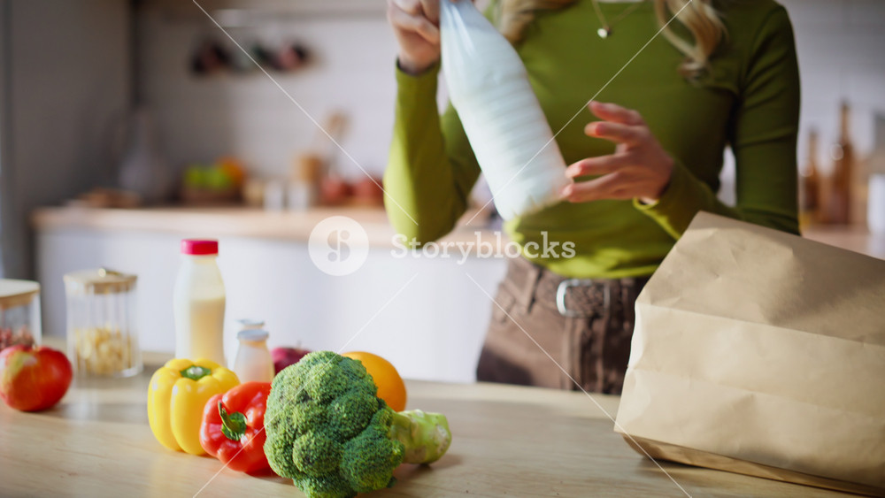 Home lady unpacking groceries from paper bags standing white kitchen interior closeup. Happy blonde woman taking healthy food from packages
