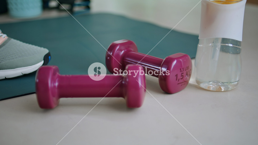 Sportswoman hands putting dumbbells on yoga mat near water bottle closeup. Unrecognizable fit woman placing sport equipment on gym floor.