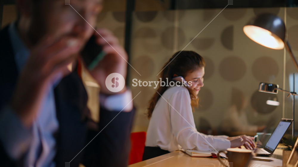 Agency coworkers calling phones working at laptops in night office closeup. Businessman businesswoman talking cellphones at dark workplace