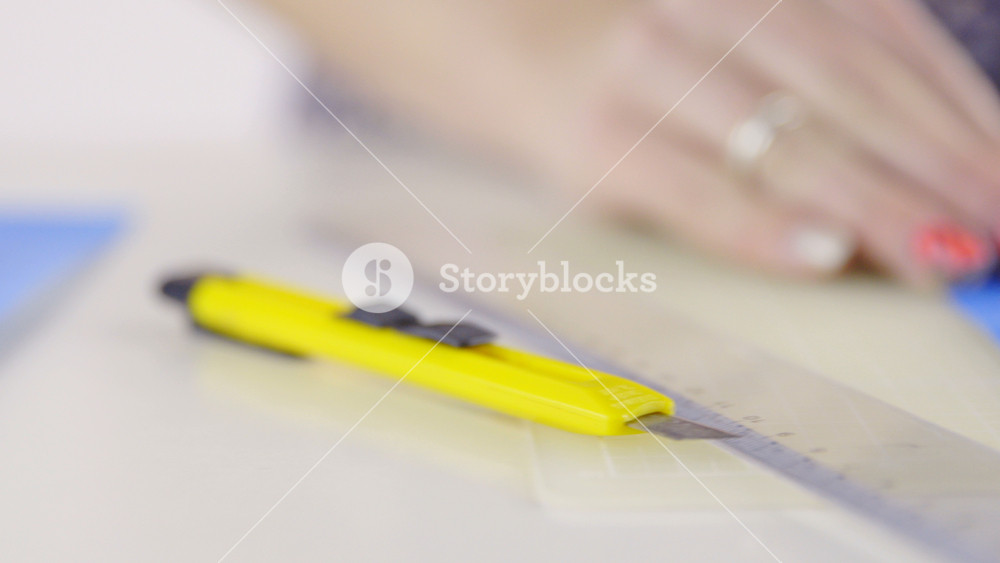 Cutting paper with knife and ruler closeup 4K. Female person with attractive colored fingernails making smaller pieces of blue paper with help of knife and ruler.