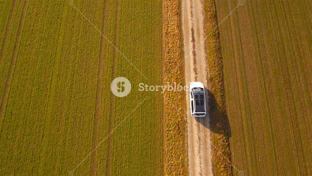 White minivan car driving beside farm fields top view drone shot 4K. Flying directly above vehicle with dark glass roof in focus driving on macadam road. Countryside landscape.