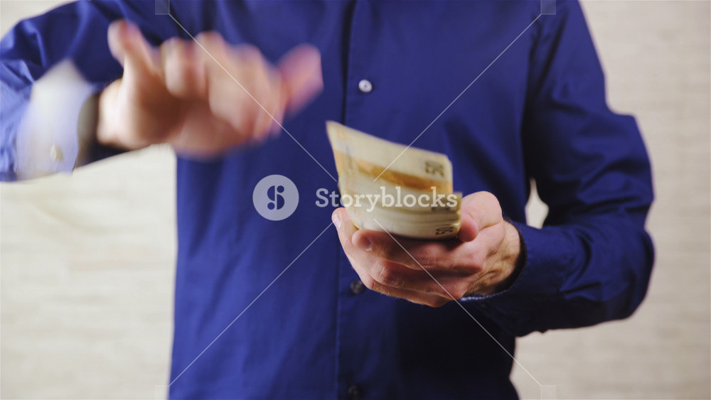 Throwing money in camera lens close up 4K. Static shot of person waist dressed in dark blue shirt putting up pack of Euro banknotes and start throwing money towards camera.