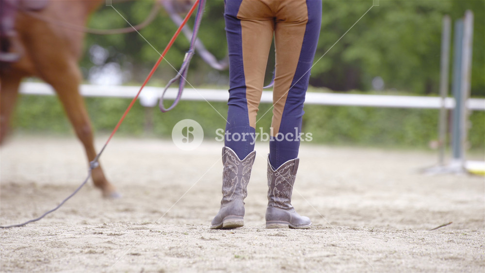 Western boots of cowgirl in manege training close up 4K. Long shot of boots in focus while person holding lunge line and whip.