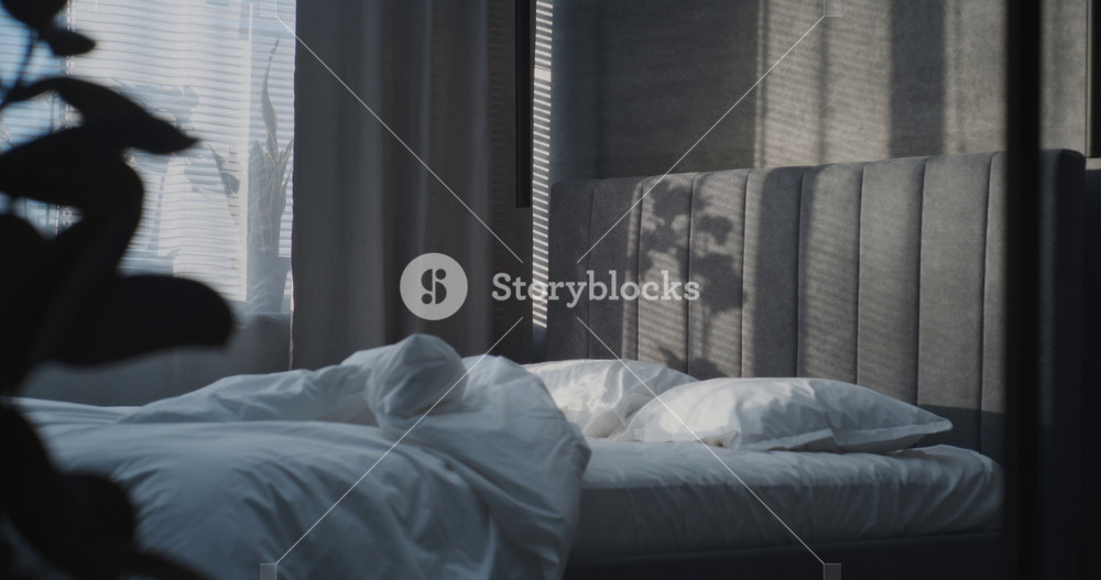 In Modern, Stylish Bedroom, Adult Man Lies Down in Bed Under Soft White Blanket, Relaxing and Preparing to Sleep. Concept of Comfort, Cozy